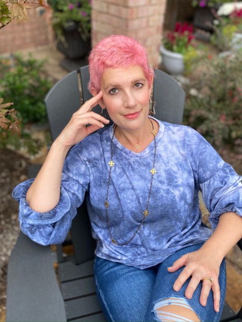 Breast cancer survivor with pink hair dyed for October smiling at camera.